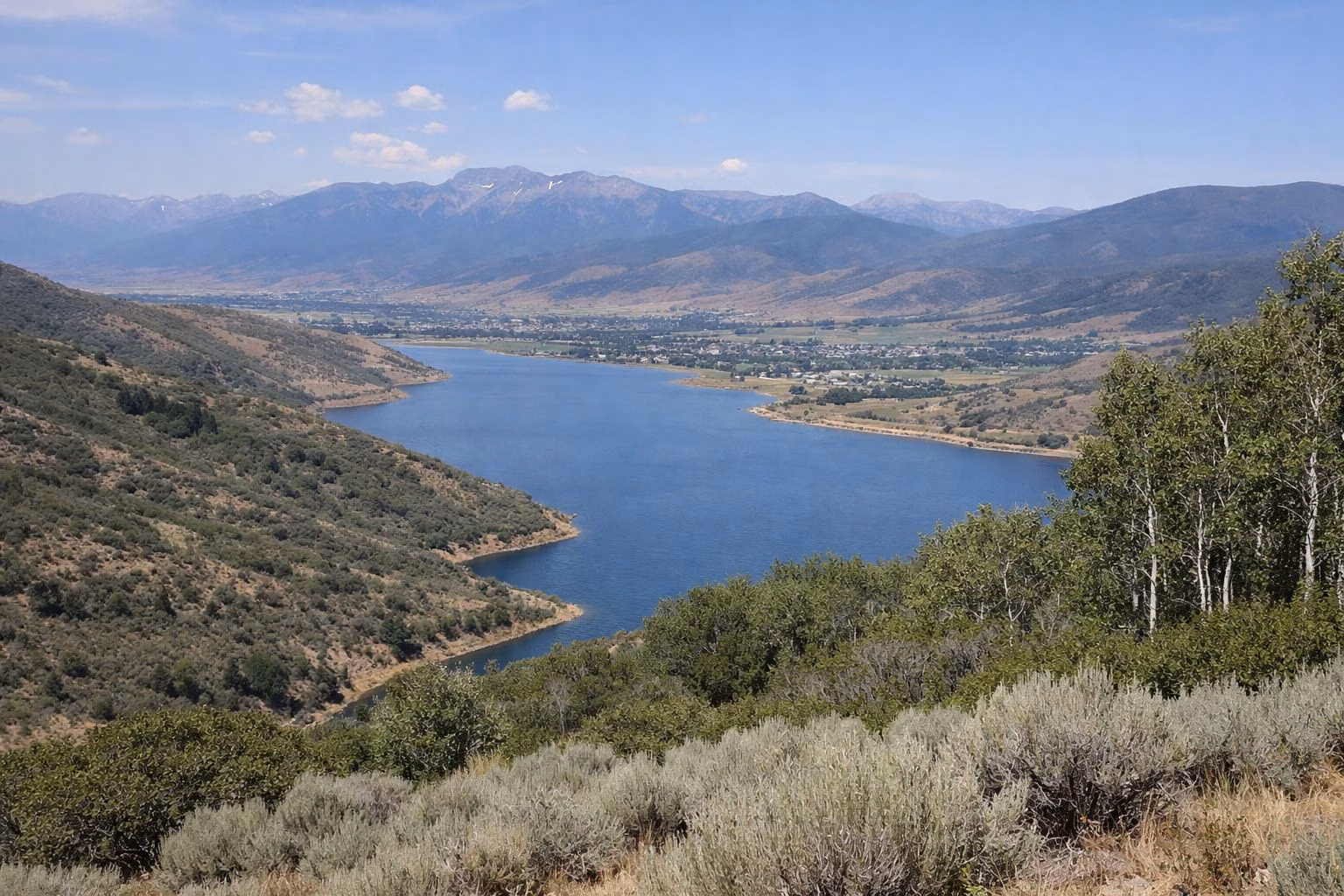 A long blue mountain reservoir filling a valley, seen from a high sagebrush hillside
