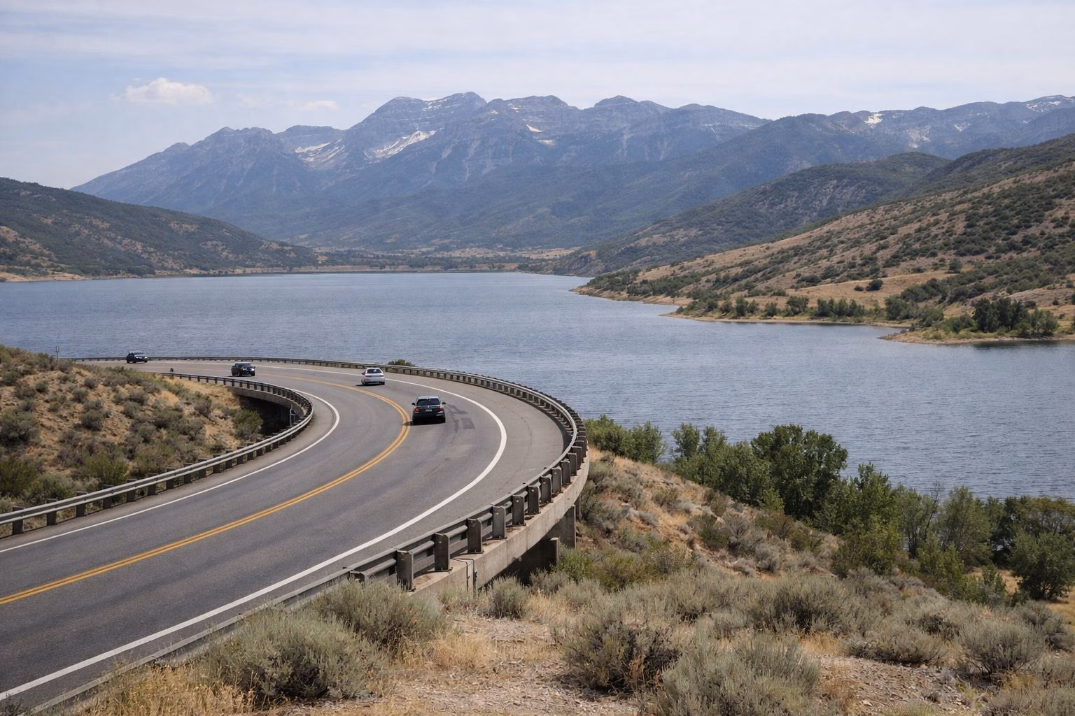 A two-lane highway curving above a large mountain reservoir and sagebrush hills