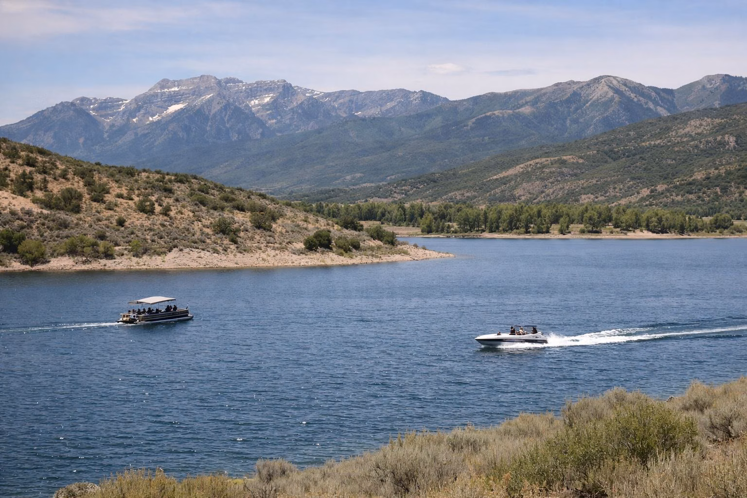 A pontoon boat and a ski boat cruising on a blue mountain reservoir with hills behind