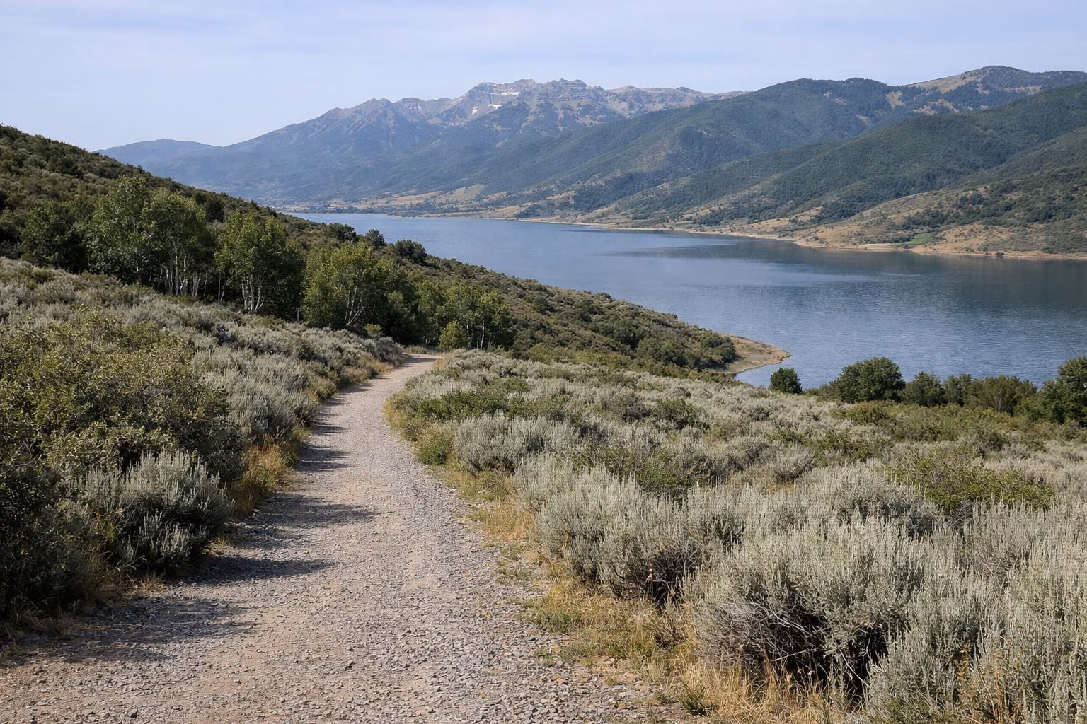 A gravel trail winding through sagebrush hills above the arm of a mountain reservoir
